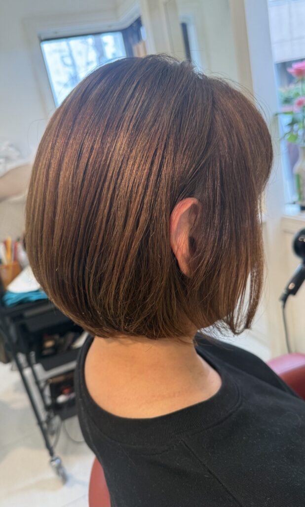 長い髪からカットした丸みボブの右斜め後ろ姿。ベージュ系カラーのやわらかな色合いと内側に収まる毛先