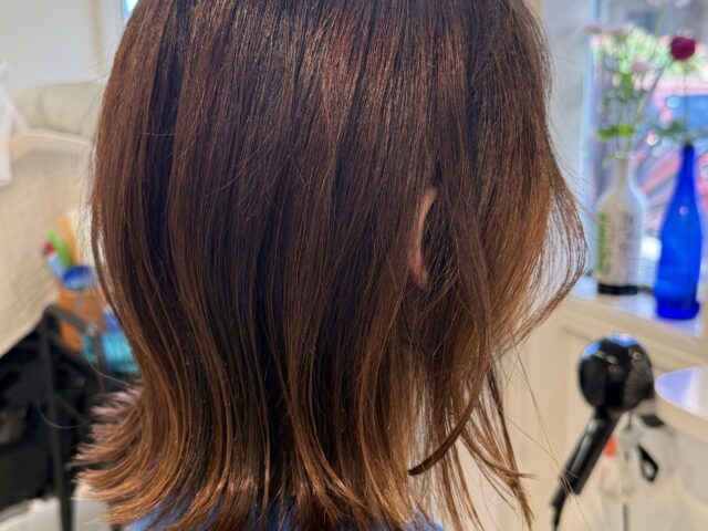 アッシュブラウンのくびれボブを横から見たスタイル。耳まわりのさりげないイヤリングカラーと外はねの毛先