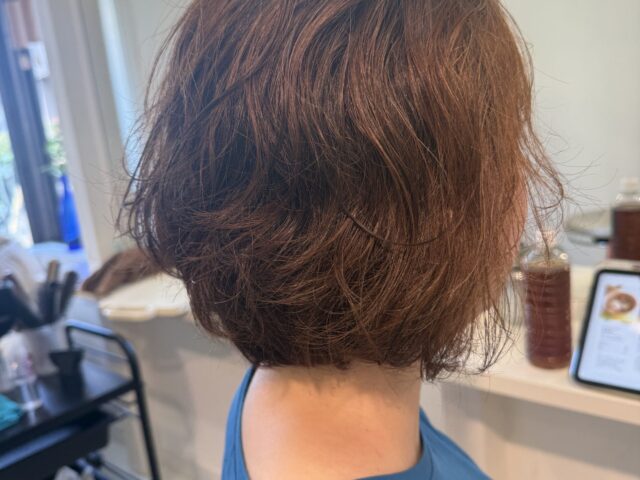大きなウェーブのパーマをかけたボブの右斜め後ろ姿。やわらかく重なる毛束と丸みのあるシルエット