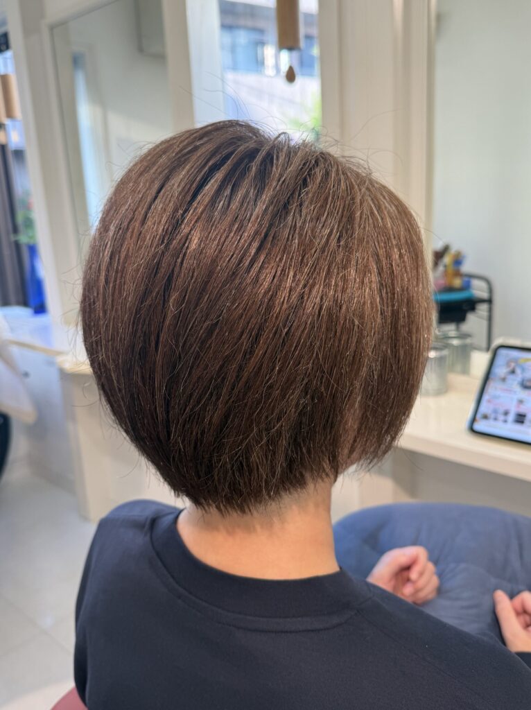 毛量が多い髪を整えたショートボブの後ろ姿。白髪ぼかしのアッシュベージュと首に沿うすっきりした襟足