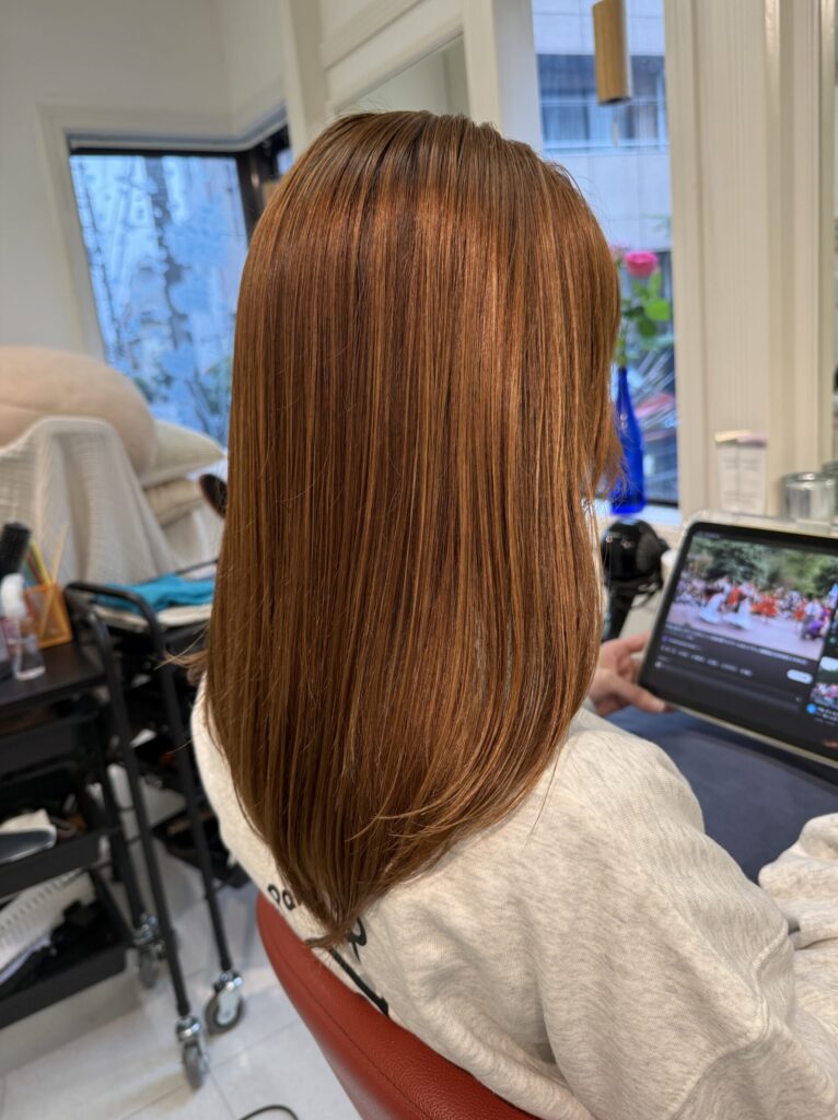 明るいアッシュベージュのロングヘアを斜め後ろから見たスタイル。ツヤのある毛流れと内側にまとまる毛先