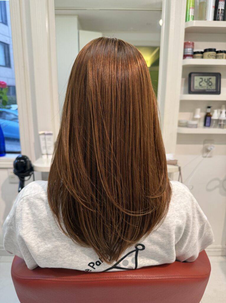 明るいアッシュベージュのロングヘアの後ろ姿。背中に沿って流れる髪と丸みのある毛先