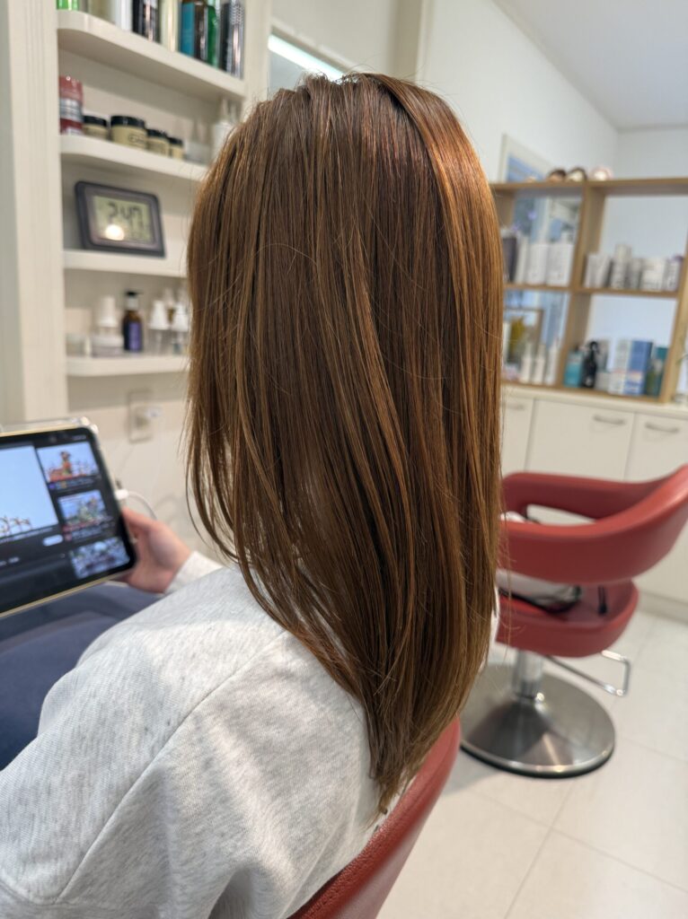 アッシュベージュのロングヘアを斜め後ろから見たスタイル。なめらかな髪の流れとやわらかな色合い