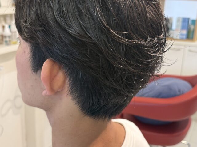 メンズパーマを左斜め後ろから見たスタイル。自然に立ち上がるトップと後ろへ流れる毛束、長さを残したツーブロック
