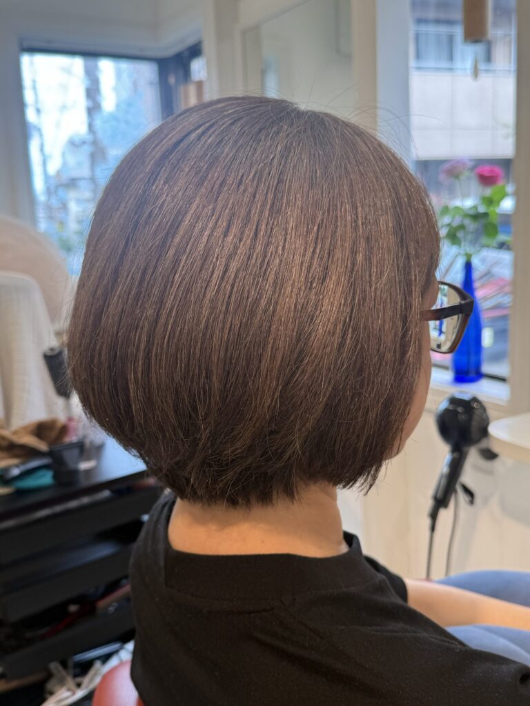 オリーブベージュのショートボブを斜め横から見たスタイル。後頭部からつながる丸みとなめらかな毛流れ